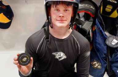 Juuso Parssinen holds up his game puck from his first NHL goal with a helmet on and a smile
